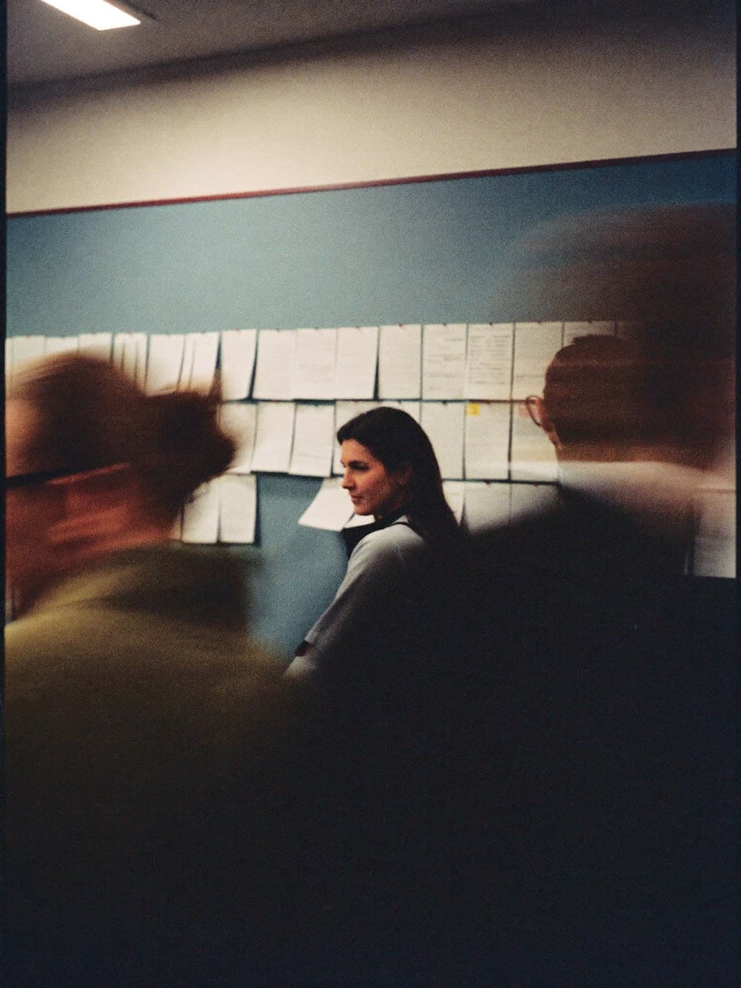 An editor standing at a wall of pinned notes while the room moves past